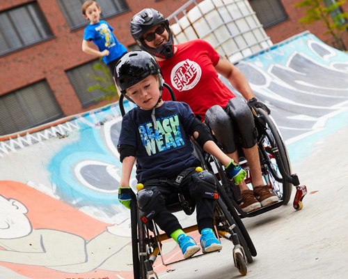 Zwei ROhllstuhlsportler mit Helm im Skatepark