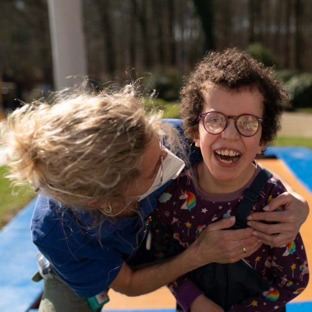 Ein Kind mit Behinderung lacht in die Kamera und wird von einer Frau gehalten