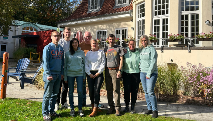 Acht Frauen und Männer stehen auf einer Rasenfläche vor dem Neuen Kupferhof