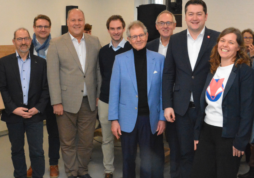 Acht Personen stehen nebeneinander in einem Raum und lächlen in die Kamera