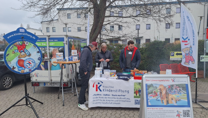 Drei Personen an einem Stand mit Infomaterial auf einem Gewerbehof