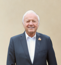 Portraitfoto von Person, die lächelnd in die Kamera schaut, neutraler Hintergrund.