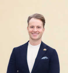 Portraitfoto von Person, die lächelnd in die Kamera schaut, neutraler Hintergrund.
