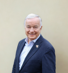 Portraitfoto von Person, die lächelnd in die Kamera schaut, neutraler Hintergrund.