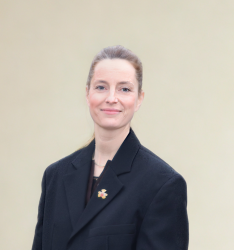 Portraitfoto von Person, die lächelnd in die Kamera schaut, neutraler Hintergrund.