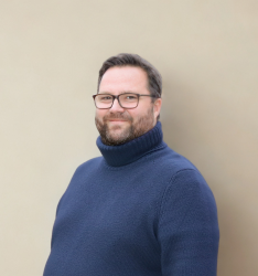 Portraitfoto von Person, die lächelnd in die Kamera schaut, neutraler Hintergrund.
