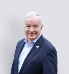 Portraitfoto von Person, die lächelnd in die Kamera schaut, neutraler Hintergrund.