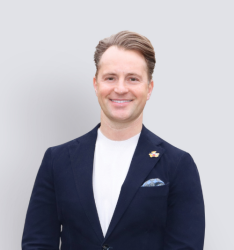 Portraitfoto von Person, die lächelnd in die Kamera schaut, neutraler Hintergrund.