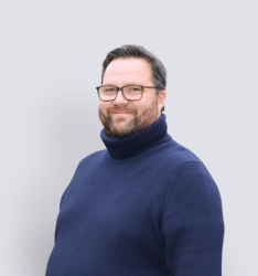 Portraitfoto von Person, die lächelnd in die Kamera schaut, neutraler Hintergrund.