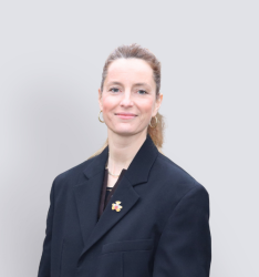 Portraitfoto von Person, die lächelnd in die Kamera schaut, neutraler Hintergrund.