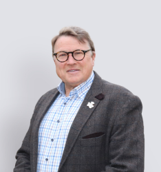 Portraitfoto von Person, die lächelnd in die Kamera schaut, neutraler Hintergrund.